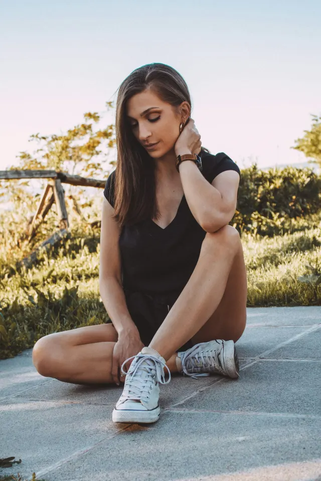 A woman sitting outdoors in a field as the sun goes down