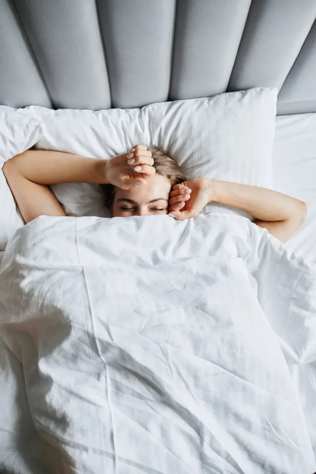 A woman stretching awake under a white duvet