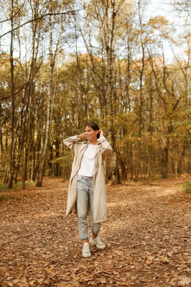A woman in a long coat on an autumn path between trees